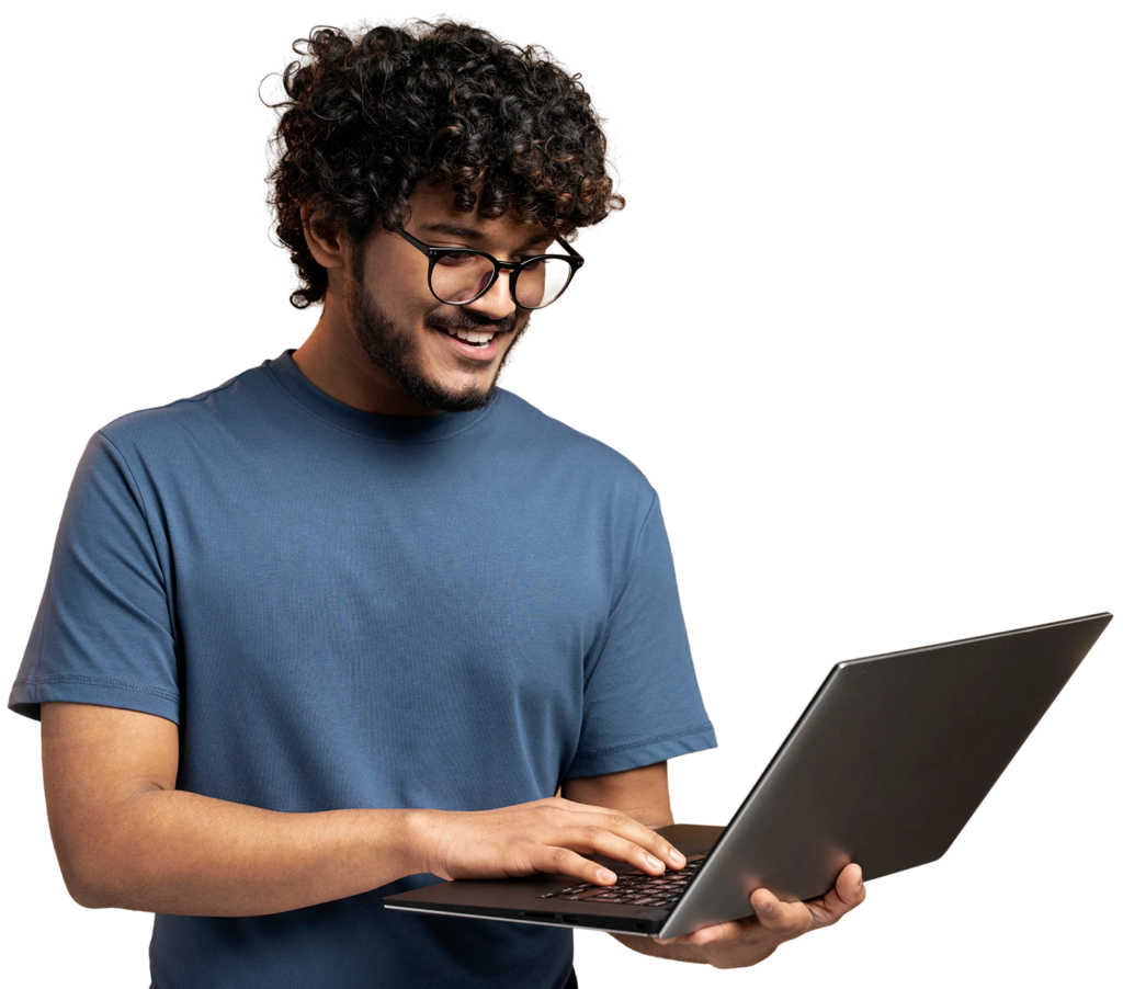 A person wearing glasses and a blue t-shirt is smiling while using a laptop.