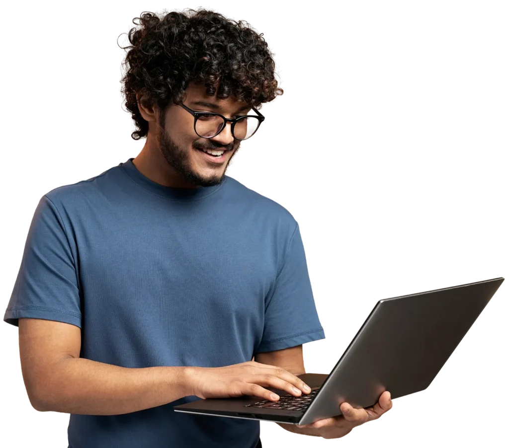 A person wearing glasses and a blue t-shirt is smiling while using a laptop.